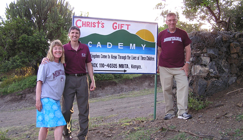 Three Griz alumni stand in front of sign outside Kenyan orphanage
